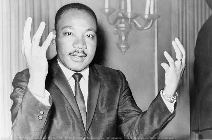 Rev. Martin Luther King, head-and-shoulders portrait, seated, facing front, hands extended upward, during a press conference